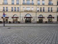 people walking on sidewalk in front of an old hotel building with large windows and doors