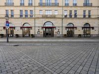 people walking on sidewalk in front of an old hotel building with large windows and doors