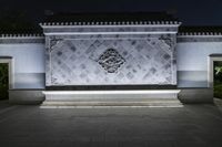 large fountain outside at night with lighting on the sides and a carved lion head, a pattern in stone