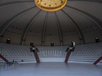 a empty auditorium with white chairs and ceiling lights, as a person stands alone in the center of it