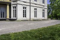 a large house with stone pillars sits along a cobblestone street next to a green lawn