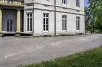 a large house with stone pillars sits along a cobblestone street next to a green lawn