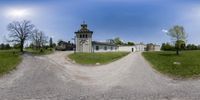 a large house with a tower sits in a grassy field with dirt roads that cross into the photo