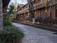 a stone sidewalk surrounded by houses and trees with lamps on it's sides in a town setting