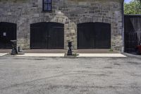 an older stone building with garage doors and two fire hydrants on each side of the driveway