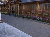 a sidewalk with flowers in pots and a building that has a fence near it and lights on