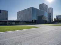 a building is on a sunny day in this photo, there is grass around the concrete area with bushes and buildings