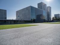 a building is on a sunny day in this photo, there is grass around the concrete area with bushes and buildings