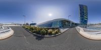 a panoramic picture shows the view from inside of an airport terminal with lots of windows, and grass and trees, and a sky