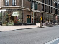 two people riding bicycles next to a storefront with many bikes on the sidewalk behind it