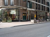 two people riding bicycles next to a storefront with many bikes on the sidewalk behind it