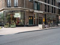 two people riding bicycles next to a storefront with many bikes on the sidewalk behind it