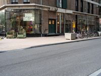 two people riding bicycles next to a storefront with many bikes on the sidewalk behind it