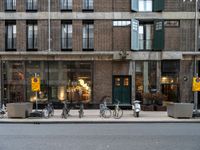 a group of bikes that are by some building facades on a street corner with a man walking next to them