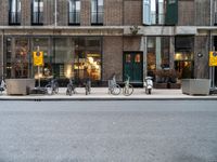 a group of bikes that are by some building facades on a street corner with a man walking next to them