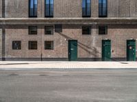 a brick building has green doors and windows and has a manhole sign in front of it