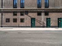 a brick building has green doors and windows and has a manhole sign in front of it