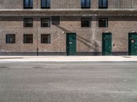 a brick building has green doors and windows and has a manhole sign in front of it