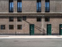 a brick building has green doors and windows and has a manhole sign in front of it