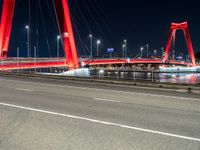 a road with lights on a bridge next to water at night with red columns and white lines