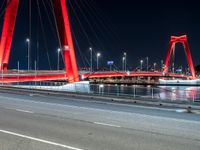 a road with lights on a bridge next to water at night with red columns and white lines