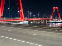 a road with lights on a bridge next to water at night with red columns and white lines