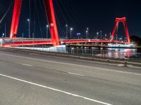 a road with lights on a bridge next to water at night with red columns and white lines