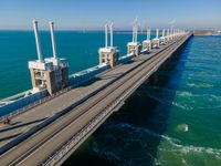 the large bridge is above the ocean next to water and wind turbine stacks in a distance