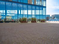 a sidewalk with several benches near tall buildings and blue windows with the word salara on them