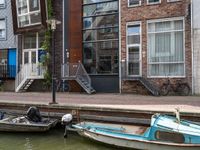 three small boats tied to the side of the canal in front of brick buildings and bicycles parked next to them