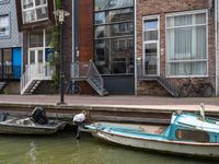 three small boats tied to the side of the canal in front of brick buildings and bicycles parked next to them