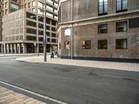 the side walk with the street next to it is empty with traffic lights on either side and buildings on the other side