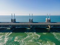 a bridge over the ocean with construction equipment in the background and two people walking on it