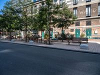 a street and an empty area with benches, a bench, and other trees surrounding the pavement