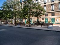 a street and an empty area with benches, a bench, and other trees surrounding the pavement