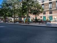 a street and an empty area with benches, a bench, and other trees surrounding the pavement