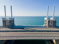 a bridge over the ocean with construction equipment in the background and two people walking on it