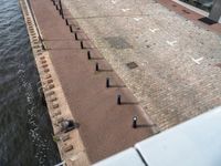 an outdoor brick walkway at a public park area beside water line that has small bars