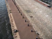 an outdoor brick walkway at a public park area beside water line that has small bars