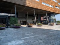 a large building with trees and potted plants near by it and a stone floor