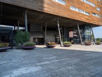 a large building with trees and potted plants near by it and a stone floor