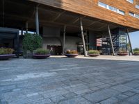 a large building with trees and potted plants near by it and a stone floor