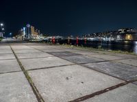 an empty sidewalk at night, with lights and the city behind it at night in london