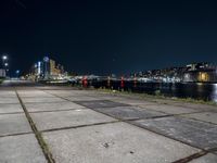 an empty sidewalk at night, with lights and the city behind it at night in london