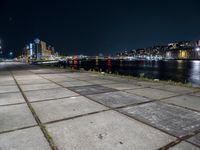 an empty sidewalk at night, with lights and the city behind it at night in london