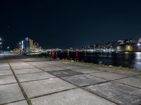 an empty sidewalk at night, with lights and the city behind it at night in london