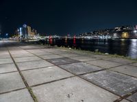 an empty sidewalk at night, with lights and the city behind it at night in london