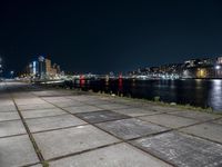 an empty sidewalk at night, with lights and the city behind it at night in london