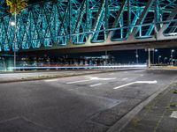 an empty city road in front of an illuminated bridge at night on a street corner