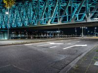 an empty city road in front of an illuminated bridge at night on a street corner